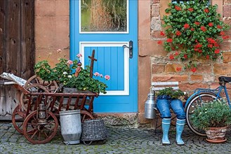 Curious decoration on a front door, blue jeans trousers in rubber boots with flower pot