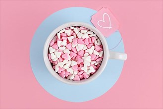 Tea cup filled with pink and white sugar hearts and label with heart on pink background,