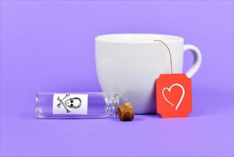 Empty open vial with cork and poison skull label next to tea cup with heart on red label on purple background,