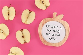 Apple halves with apple shaped picture frame with text An apple a day keeps the doctor away on pink background,