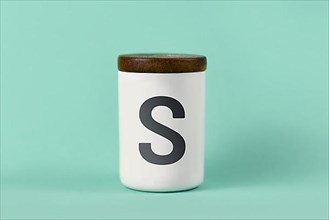 White salt shaker with wooden lid and letter S on green background,