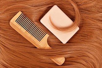 Solid shampoo bar and wooden comb on red hair. Concept for eco friendly healthy hair care routine,