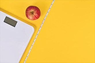 Dieting concept with scale, measuring tape and apple on yellow background with copy space