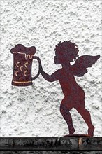 Iron rusty putto with beer stein in front of house wall, Hindelang