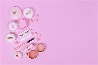 Pink makeup beauty products like brushes, powder or lipstick on side of pastel pink background with empty copy space