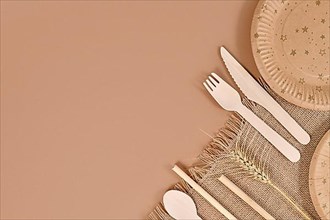 Eco friendly paper party plates and wooden cutlery in corner of beige background with copy space,