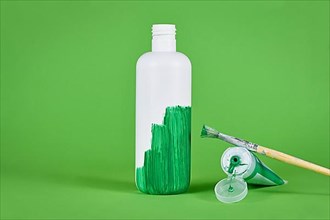 Greenwashing concept with white plastic bottle being painted green,
