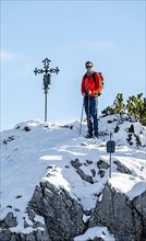 Mountaineer next to summit cross of Weitalpspitz in winter with snow, Ammergau Alps