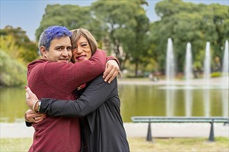 Cheerful queer couple hugging in a park looking at the camera,