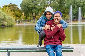 Gay Latino male couple sitting on a bench in a park laughing,