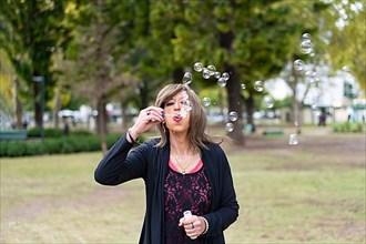 Mature trans woman blowing bubbles in a park,