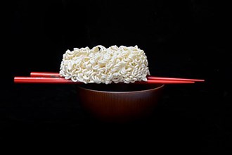 Dried Asian noodles on chopsticks with bowl, pasta