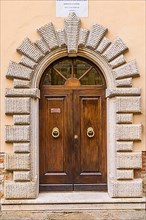 Round arched house entrance door framed with cream-coloured stones, Montefollonico