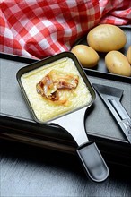 Raclette, melted raclette cheese with bacon in pans and ingredients