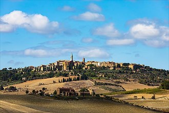 Country house behind ploughed field, behind it the panorama of Pienza