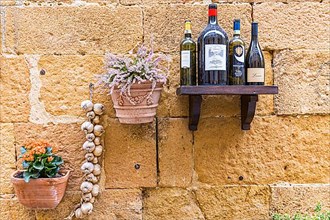 Wine bottles, flower box and garlic as decoration on a house wall in the centre of Pienza