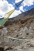 Small white stupa on the mountainside, prayer flags in front