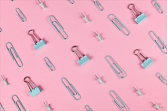 Stationery items like paper clips and drawing pins arranged on pink background,