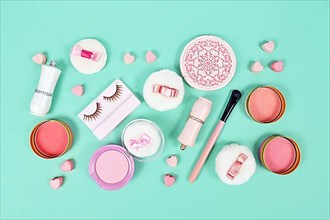 Cute pink makeup beauty products like brushes, powder or lipstick on teal blue background