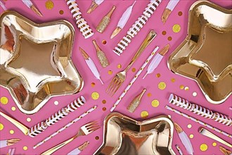 Party flat lay with golden and white decoration like plates, confetti and feathers on pink background