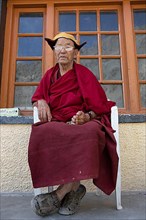 Monk sitting on garden chair, Buddhist Yellow Cap Monastery Rizong or Rhizong or Yuma Changchubling