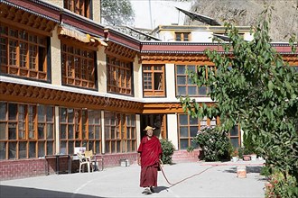 Monk with garden hose in the monastery courtyard, Buddhist Yellow Cap Monastery Rizong or Rhizong or Yuma Changchubling