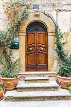 Round arched house entrance door above a stone staircase, decorated with flower pots