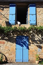 Cat sitting in an open window with blue shutters, Montignac-Lascaux