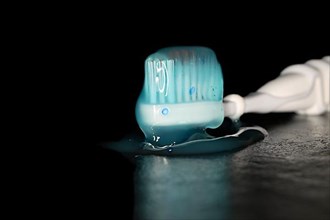 Electric toothbrush with a blue transparent toothpaste, studio photography with black background