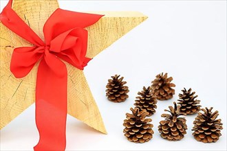 Christmas wooden star with a red bow on a white background, pine cone or pine cone on the side