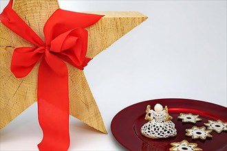 Christmas wooden star with a red bow detached against a white background, on the side a tray with a crochet angel