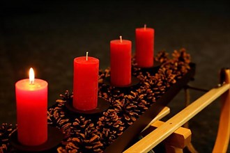 Four Advent candles decorated with pine cones on a sleigh, First Advent one candle burning