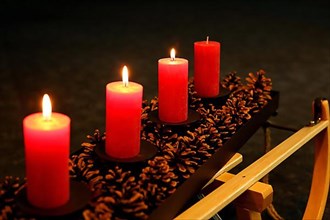 Four Advent candles decorated with pine cones on a sleigh, Third Advent three candles burning