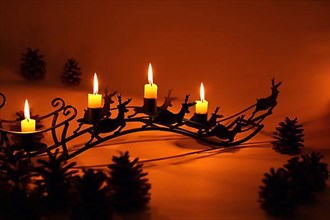 Fourth Advent with four lit candles on a sleigh with reindeer in diffuse red light,