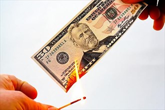 Lighting a fifty dollar note on fire and burning it. Released against a white background,