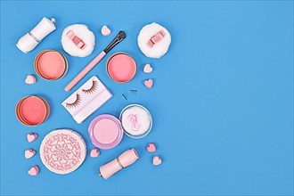 Pink makeup beauty products like brushes, powder or lipstick on side of blue background with empty copy space