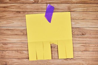 Yellow empty tear-off stub paper note without text on wooden wall,