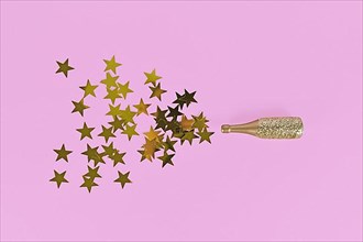 Golden star confetti splashing out of Champagne bottle on pink background,