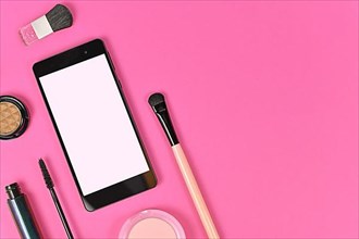 Flat lay with blank black smart phone with empty white screen and makeup beauty products on pink background with empty copy space on right side,