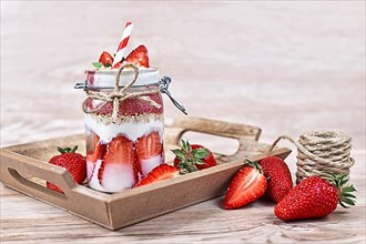 Strawberry fruit dessert with low fat yogurt, chia seeds and puffed quinoa grains layered in jar surrounded by berries on wooden background