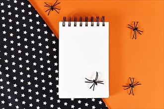 Halloween flat lay with empty notepad and spiders on orange and black background with stars,