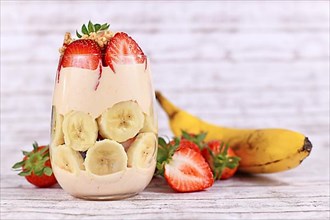 Healthy banana and strawberry fruit summer dessert with yogurt and granola layered in glass surrounded by fresh ingredients,
