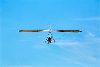 Motorised hang glider flying in slightly cloudy sky, text free space