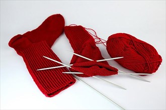 Self-knitted red socks made of wool isolated against a white background with knitting needle and ball of wool,