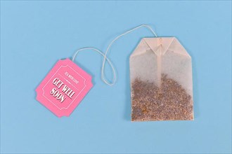 Tea bag with made up cute pink label with text Get well soon on pastel blue background,