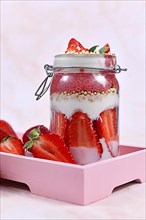Strawberry fruit dessert with yogurt, healthy chia seeds and puffed quinoa grains layered in jar surrounded by berries on pink wooden tray