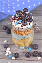 Blueberry snack made from yogurt and banana and healthy fruits topped with star shaped sugar and chocolate sprinkles in jar on wooden background,