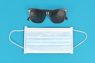 Concept for Summer during Coronavirus crisis with face mask and sunglasses on blue background,