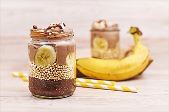 Layered healthy dessert with banana fruit slices, puffed quinoa grain and chocolate chia seed pudding in jar