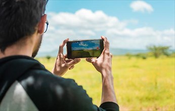 Rear view of a person taking a photo of a field with his cell phone, rear view of a man taking photos of a field